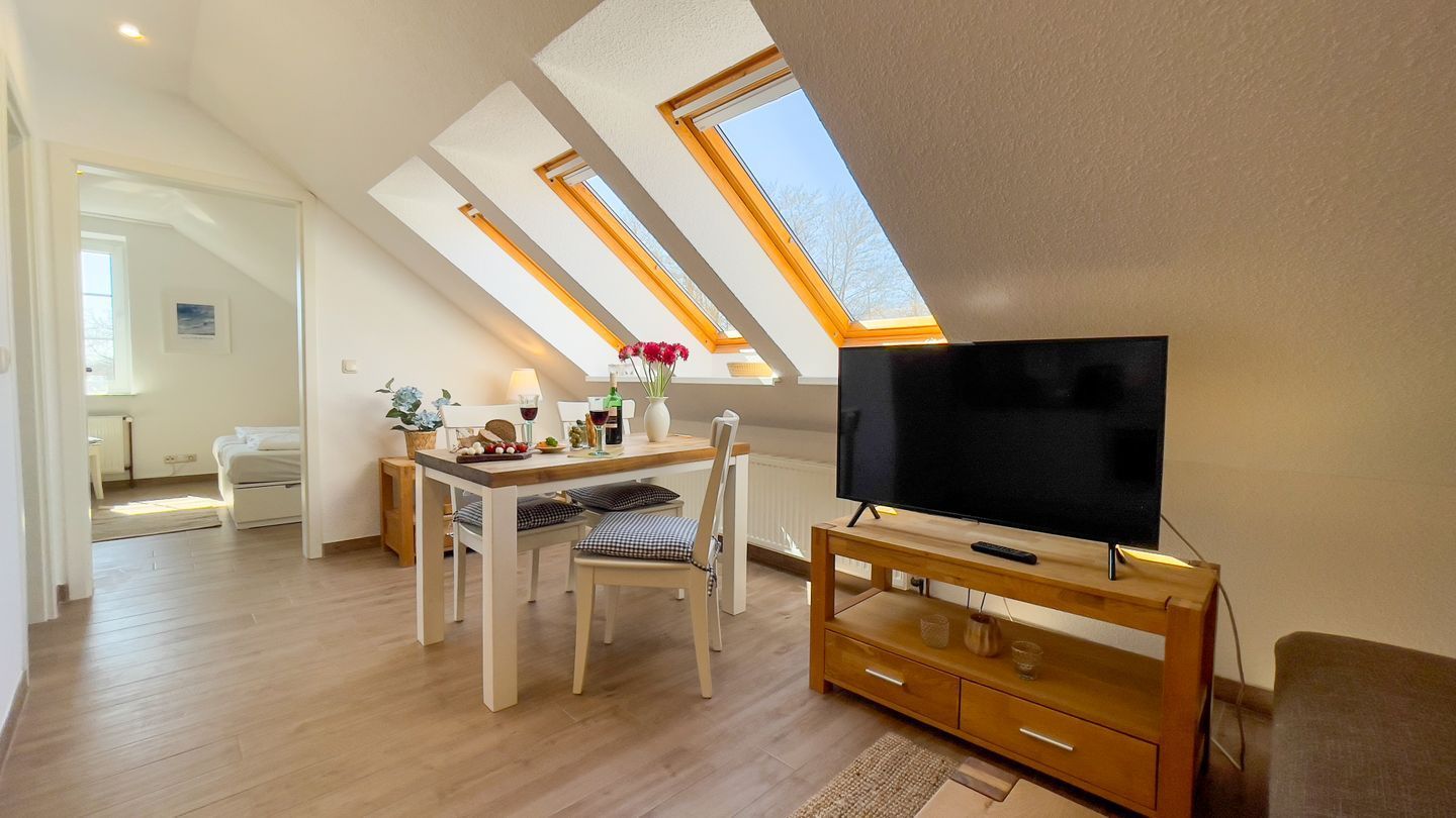 Ein modernes Wohnzimmer mit Fernseher auf einem Holzschrank, einem Esstisch mit Stühlen und einem Oberlicht.