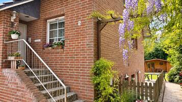 Ein Ziegelhaus mit einer Holzveranda, einer Treppe und einem Garten mit violetten Blumen.