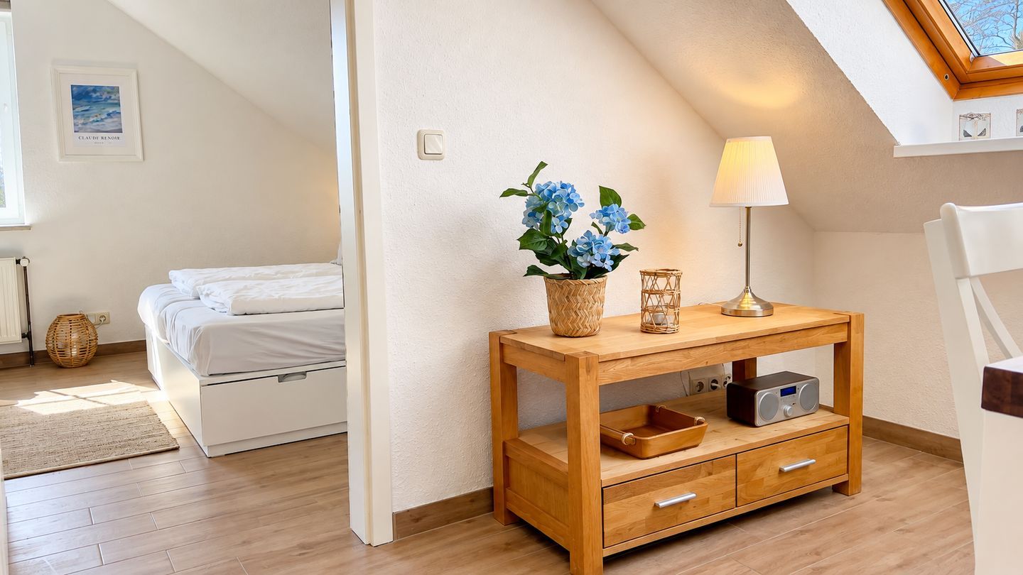 Ein Schlafzimmer mit einem Bett, einem Nachttisch mit Lampe, einem Radio und einer Vase mit Blumen.