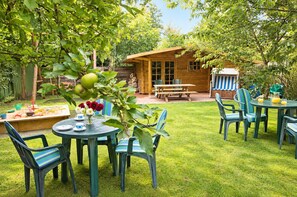 A wooden cabin with a picnic table and chairs, surrounded by a well-maintained lawn and trees.