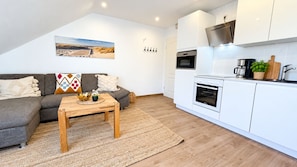 A modern living space with a sofa, coffee table, and kitchen area including an oven and microwave.