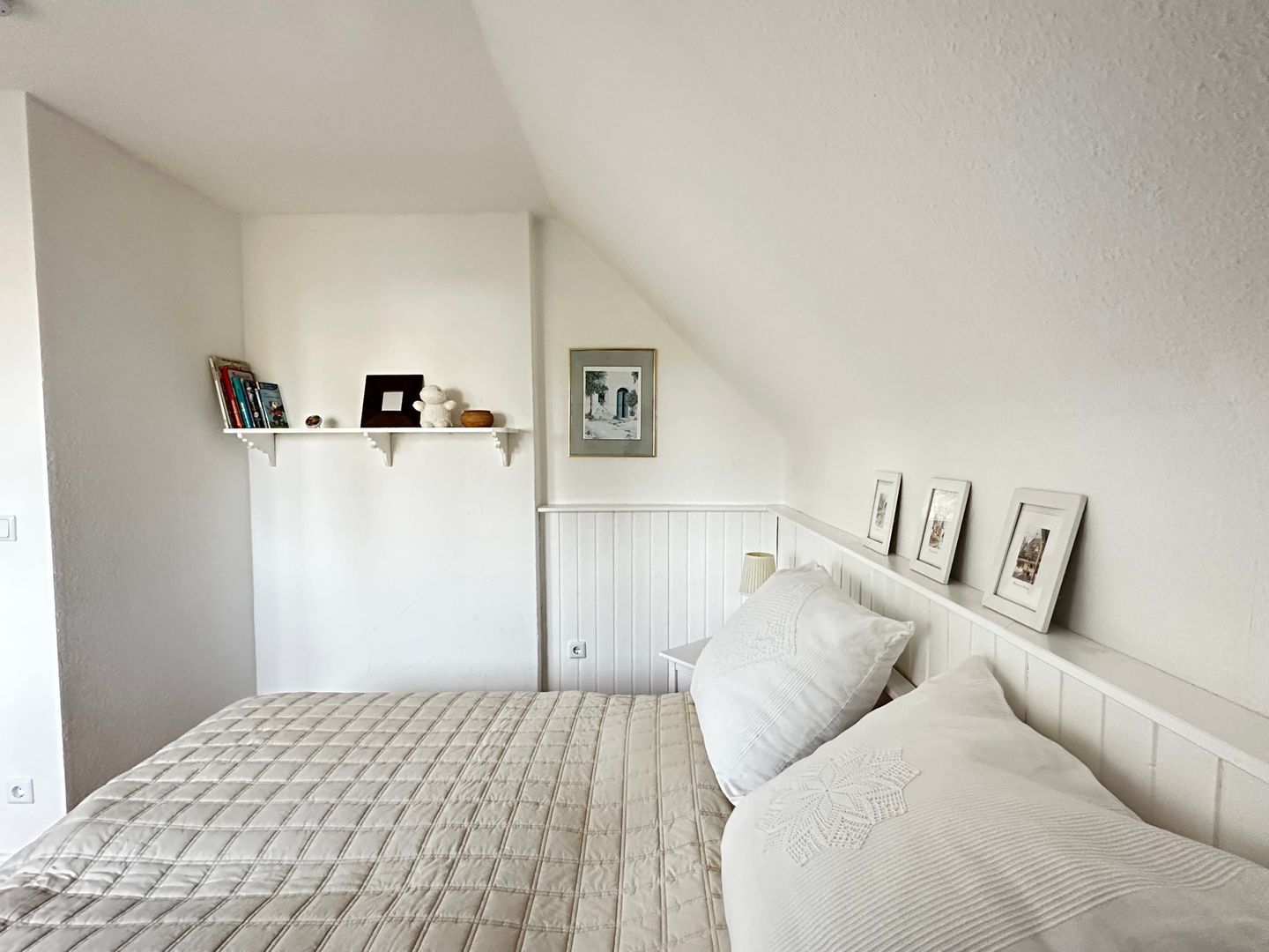 Ein Schlafzimmer mit einem Bett, einem Regal mit Büchern und einem Teddybären, einem gerahmten Bild und einem Heizkörper.