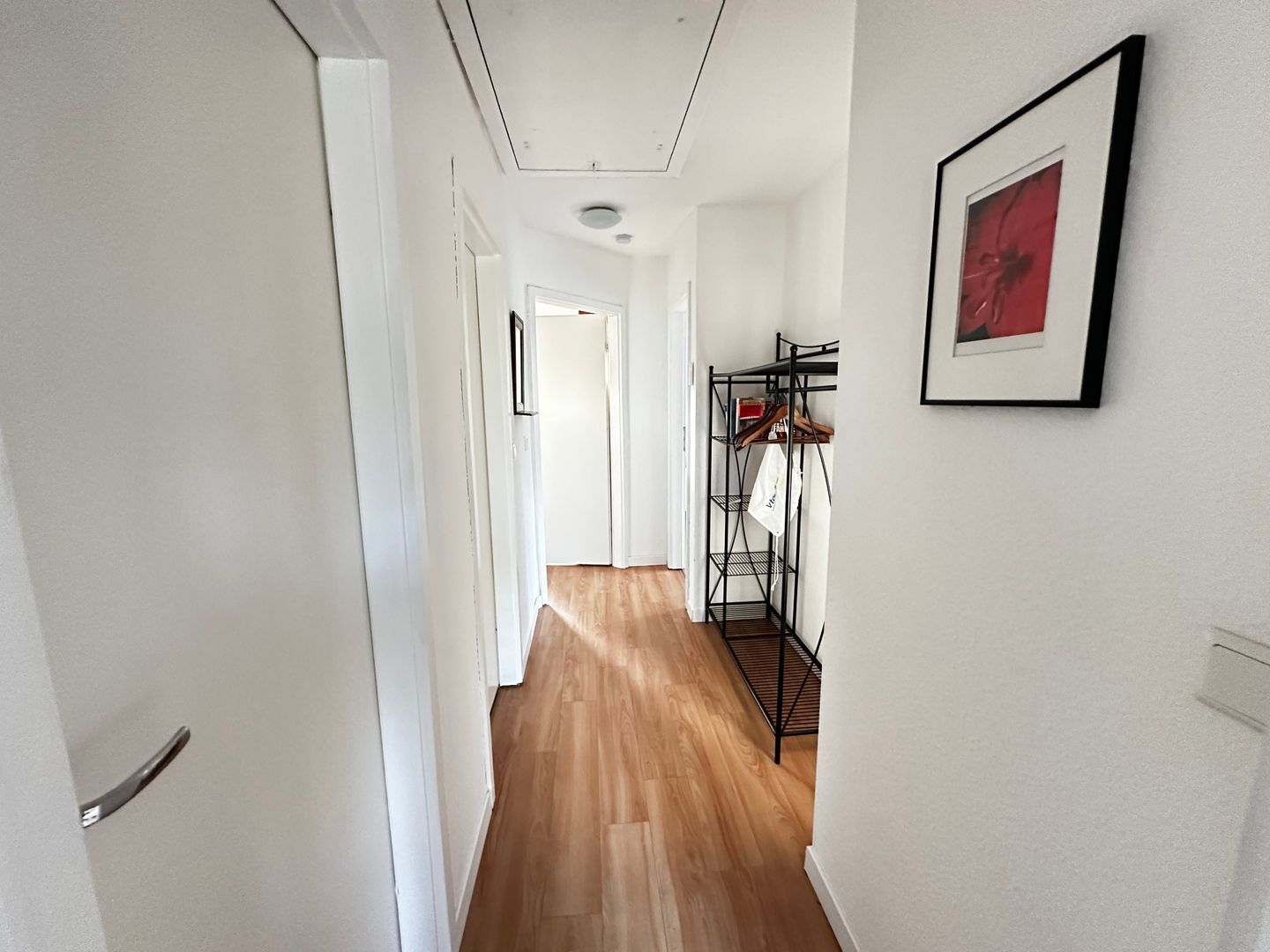 Ein Flur mit Holzboden, einem Metallgestell mit Kleidung und einem gerahmten Bild an der Wand.