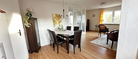 A dining area with a table set for four, a chandelier, and a view of the outdoors through a window.