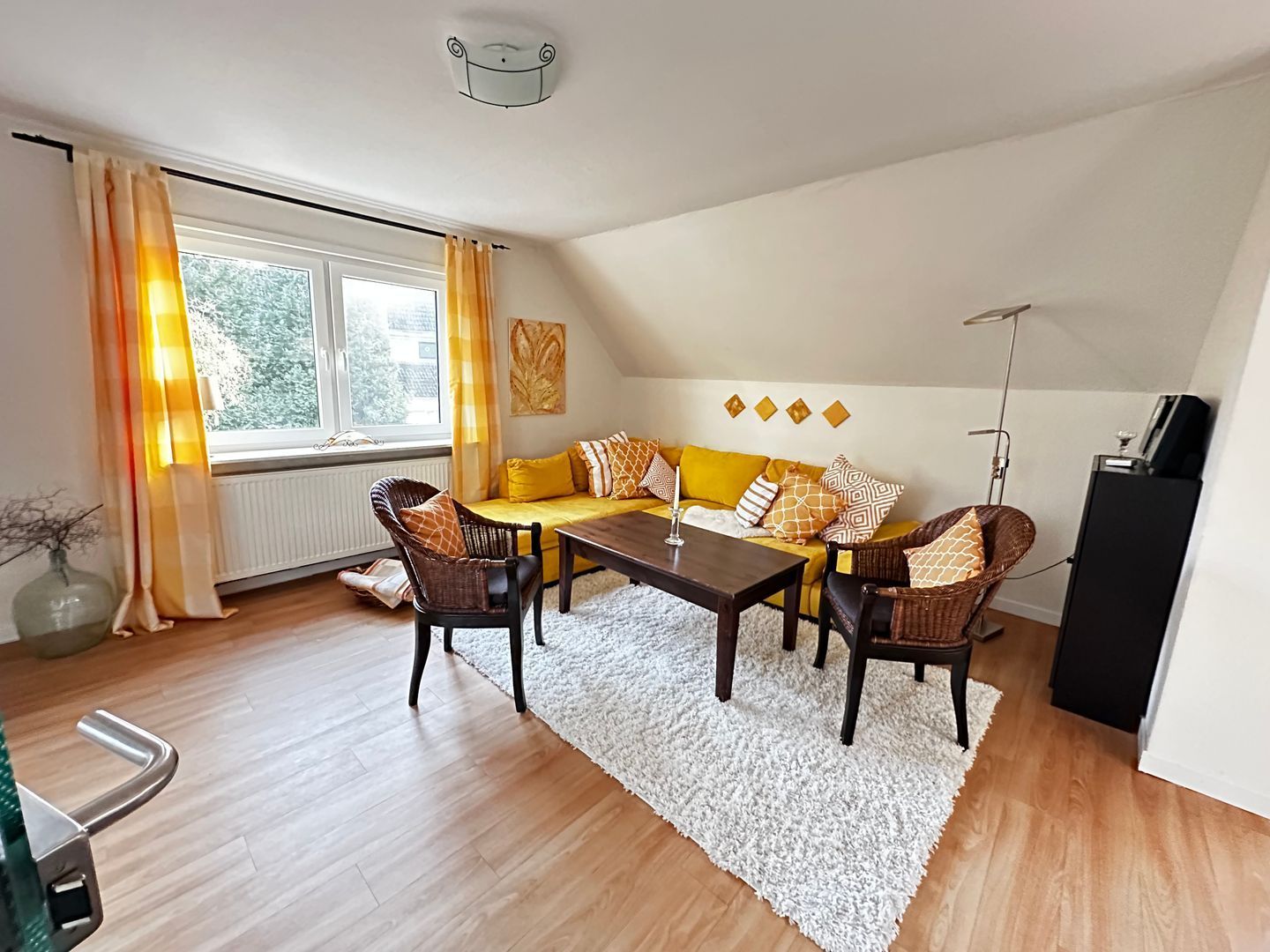 Ein Wohnzimmer mit einer Couch, Sesseln, einem Couchtisch, einer Heizung, einem Fenster mit Vorhängen und einer Lampe.