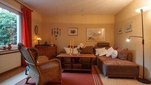 A cozy living room with a sofa, a wicker chair, a wooden coffee table, and a floor lamp. - Großzügige, Gemütliche Ferienwohnung für bis zu 6 Personen mit 3 Terrassen - Haus Wexler (Cuxhaven)