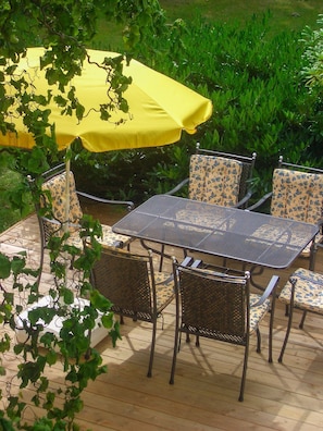 An outdoor patio with a table and chairs, a yellow umbrella, and greenery in the background.