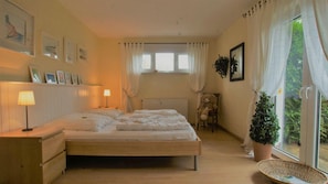 A bedroom with a bed, bedside lamps, a chair, a window with curtains, and a potted plant.