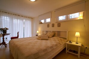 A bedroom with a large bed, a bedside table with a lamp, a chair, and a window with curtains. - Großzügige, Gemütliche Ferienwohnung für bis zu 6 Personen mit 3 Terrassen - Haus Wexler (Cuxhaven)