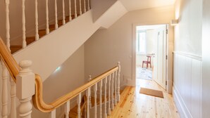 A staircase with white balusters and wooden handrails, leading to a room with a door and a small stool. - D&S -JB Apartments - B (Oporto)