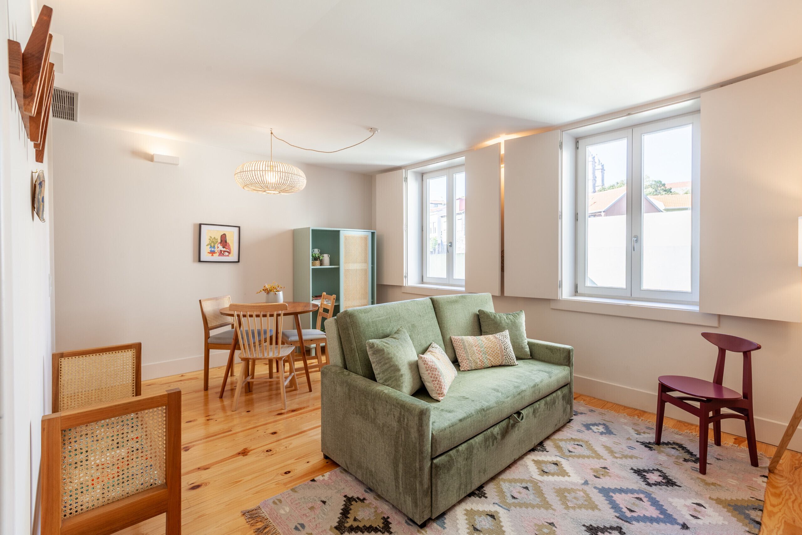 A living room with a green sofa, wooden chairs, a dining table, and a patterned rug.