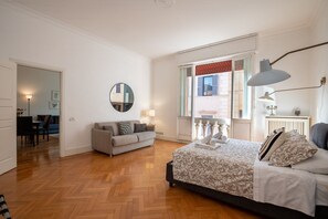 Een slaapkamer met een bed, een bank, een ronde spiegel en een raam met uitzicht.