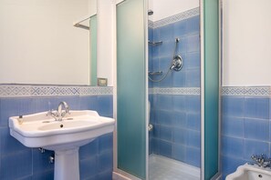 Een badkamer met een wit wastafelmeubel, een douche met een glazen deur en blauwe betegelde wanden.