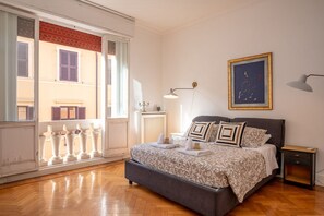 A bedroom with a bed, bedside table, lamp, and a window with a view of buildings.