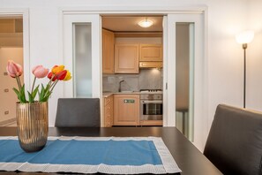 Een eethoek met een tafel, stoelen, een vaas met bloemen en uitzicht op een keuken met kasten en apparatuur.