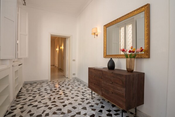A hallway with a tiled floor, a wooden dresser, a mirror, and a vase with flowers. - NinetyOne Sistina Apartment, Spanish Steps (Roma)