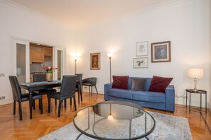 Een moderne woonkamer met een eethoek, een blauwe bank en een glazen salontafel.