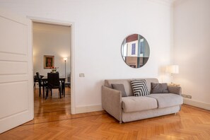 A living room with a sofa, a round mirror, a lamp, and a dining area with chairs and a table.