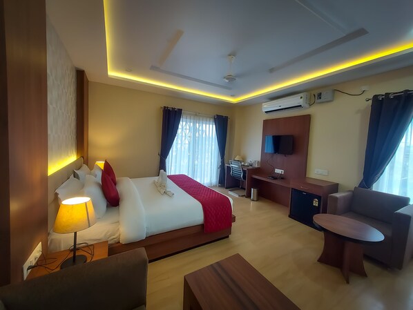 Una habitación de hotel con cama, escritorio, silla, televisión y aire acondicionado.