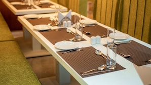 Un restaurante con largas mesas dispuestas para comer, sillas tapizadas de verde e iluminación colgante moderna.