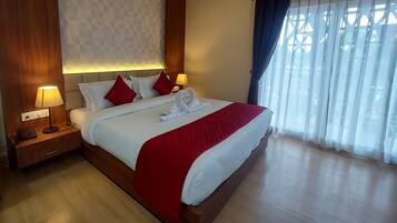 Habitación de hotel con una cama grande, dos lámparas de noche, una mesita de noche de madera y una ventana con cortinas traslúcidas.