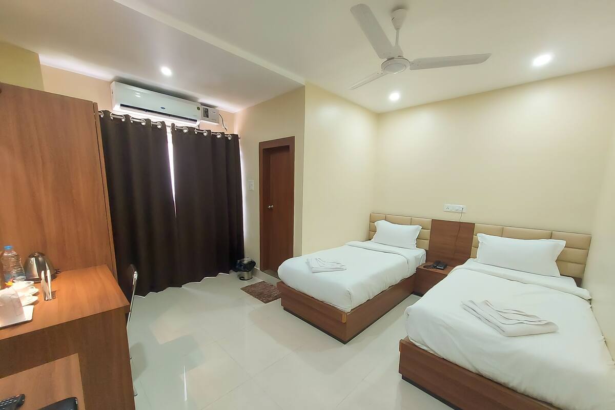 A hotel room with two beds, a desk, a ceiling fan, an air conditioning unit, and a door.