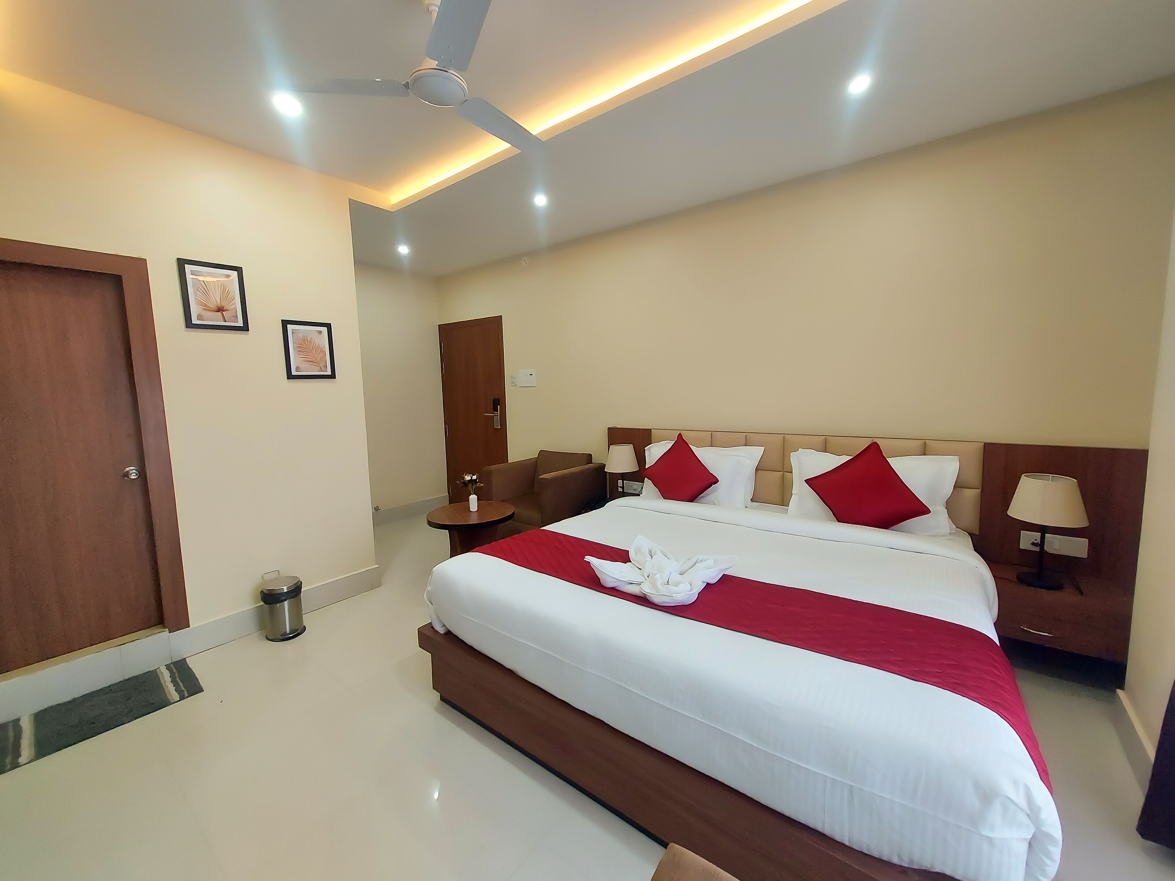 A hotel room with a large bed, a ceiling fan, bedside lamps, and a small table with a vase.