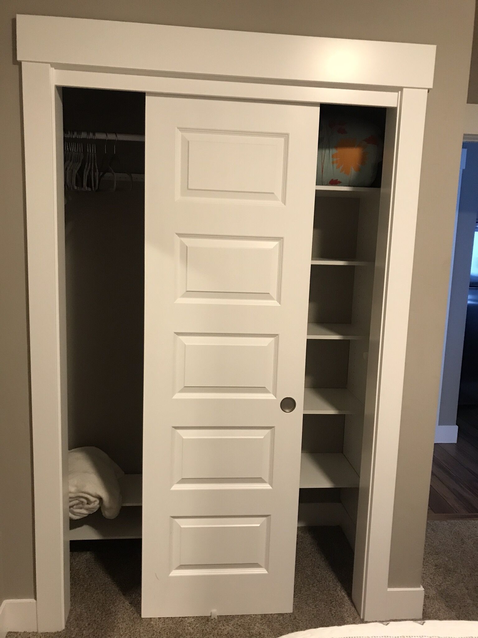 Ein weißer Kleiderschrank mit Schiebetür, einer Kleiderstange und einem Regal mit einem dekorativen Gegenstand.
