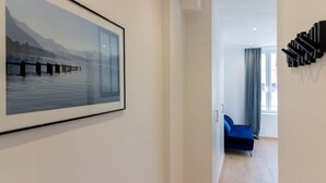 Ett modernt hotellrum med en stor, inramad tavla som föreställer en sjö, en blå soffa och ett unikt svart konstverk på väggen.