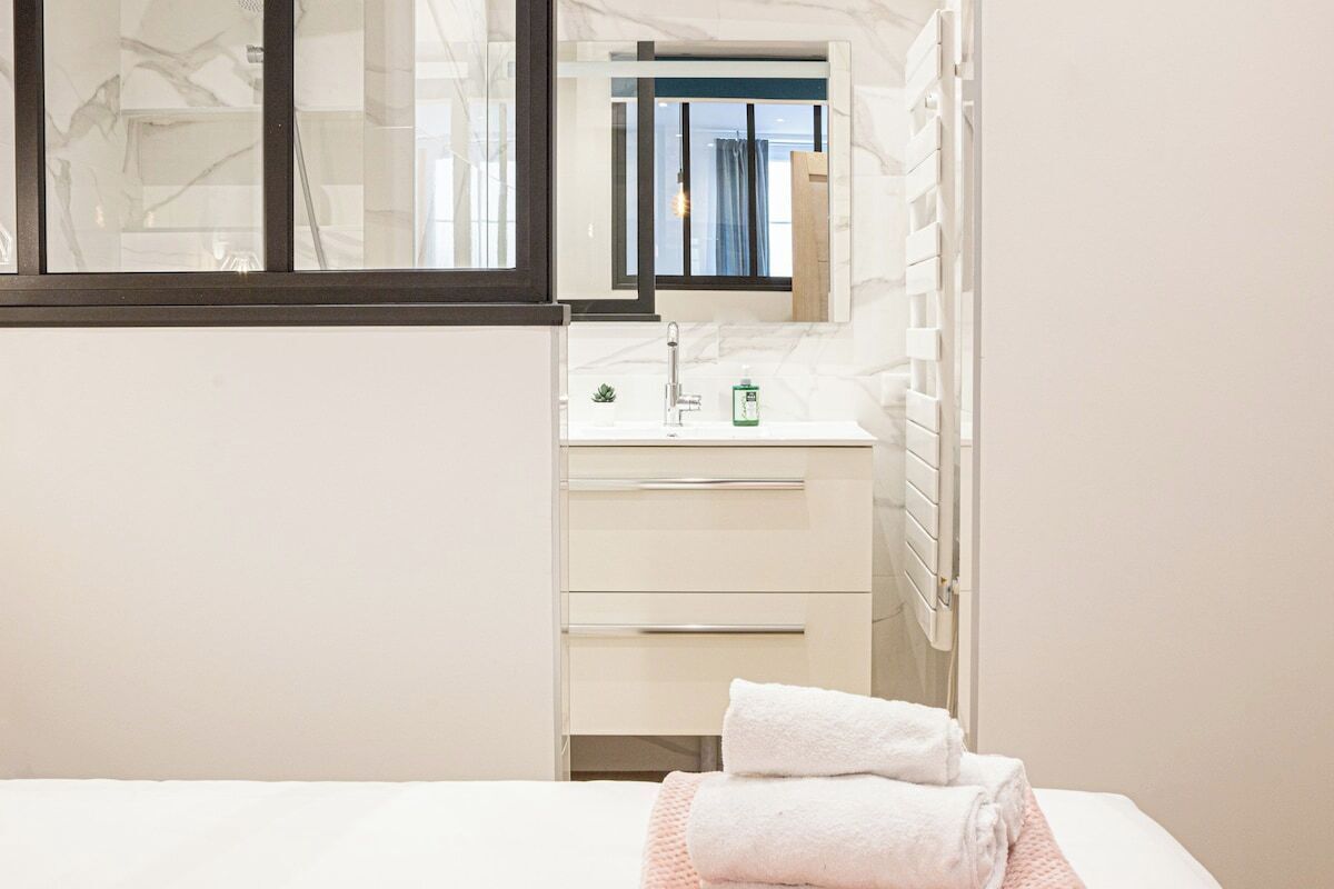 Une chambre d’hôtel avec un lit, une salle de bain blanche avec un miroir, un lavabo et une fenêtre.