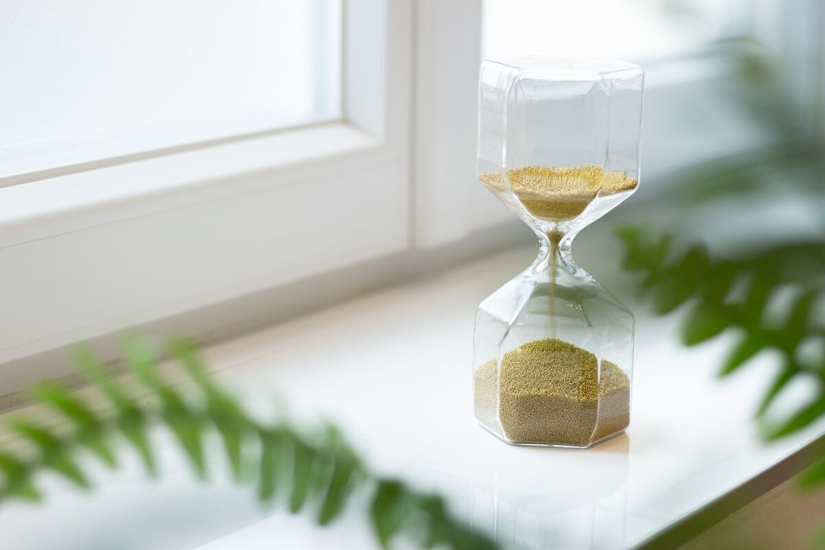 Un reloj de arena sobre un alféizar con vista a una ventana y una planta.