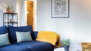 Ein Wohnzimmer mit einem blauen Sofa, einer gelben Decke und einem gerahmten Bild an der Wand.