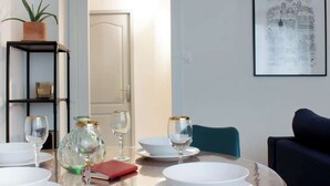 Ein Essbereich mit Tisch für vier Personen, einem Blumentopf, einem gerahmten Bild an der Wand und einer Tür im Hintergrund.