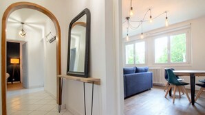 Ein modernes Interieur mit einem großen Spiegel, einem Essbereich mit Tisch und Stühlen, einem blauen Sofa und einem Fenster mit Tageslicht.