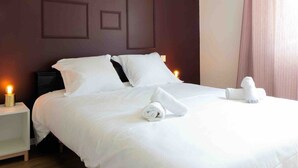 Ein ordentlich bezogenes Bett mit weißen Leinen und aufgerollten Handtüchern, eine Nachttischlampe und ein dunkler Nachttisch.