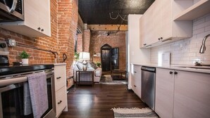 A compact kitchen with a brick wall, wooden flooring, and modern appliances.