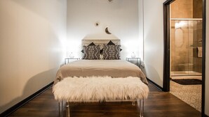 A bedroom with a bed, a ceiling fan, a nightstand, and a bathroom visible through an open door.