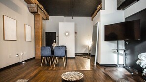 A modern interior with a wooden dining table, two blue chairs, a round woven rug, and a flat-screen TV mounted on the wall.