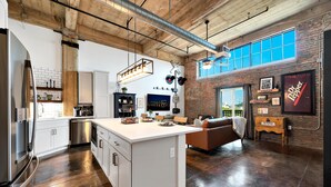 A modern kitchen with white cabinetry, a central island, and a dining area with a brown sofa. - The Crossing at 202- Downtown Waco/ Steps to Silos (Waco)