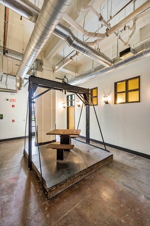 Une pièce spacieuse avec des conduits apparents, une table en bois et des lampes fixées au mur.