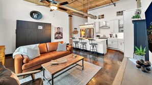A modern kitchen with a central island, bar stools, and a stainless steel refrigerator. - The Crossing at 202- Downtown Waco/ Steps to Silos (Waco)