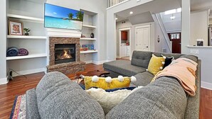 A spacious living room with a fireplace, a large TV, and a balcony.
