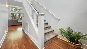 A staircase with white railings leading to a second floor, a wooden floor, and a potted plant on the landing.