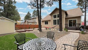 A patio with a round table and chairs, a hammock, and a house in the background.