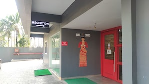 Uma área de recepção com sinalização indicando o caminho para a recepção, um letreiro de boas-vindas e uma porta vermelha.