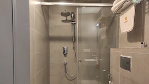 Um chuveiro compacto com porta de vidro, chuveiro manual, torneira fixada na parede e vaso sanitário.