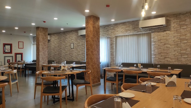 Um restaurante com várias mesas e cadeiras, decoração de parede de pedra e iluminação embutida no teto.