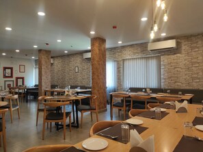 A restaurant with multiple dining tables and chairs, stone wall decor, and recessed ceiling lighting. - NK Hotel - Guwahati (Guwahati)