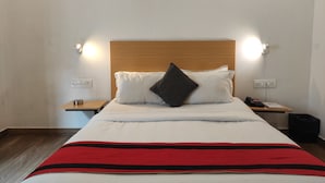 Uma cama bem arrumada com cabeceira de madeira, duas mesas de cabeceira com abajures e um cobertor listrado em vermelho.