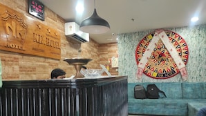 Uma área de recepção de hotel com um balcão de madeira, um relógio digital e um painel decorativo na parede.